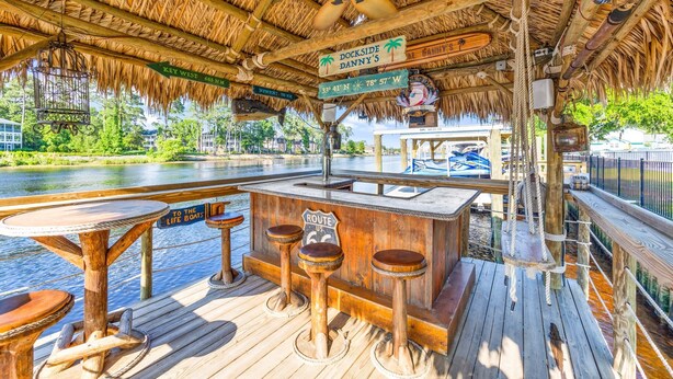 A wooden deck with a thatched roof, a bar area with stools, and a sign indicating 'Dockside Danny's' with a view of the water. - 3 Level Home on Waterway w/ Heated Pool & Hot tub (Myrtle Beach)