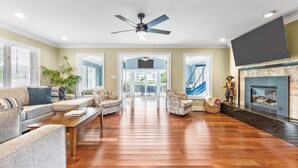 A spacious living room with a fireplace, a ceiling fan, and a large TV. - 3 Level Home on Waterway w/ Heated Pool & Hot tub (Myrtle Beach)