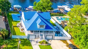 A lakeside property with a large house featuring a blue roof, a swimming pool, and a dock with boats. - 3 Level Home on Waterway w/ Heated Pool & Hot tub (Myrtle Beach)