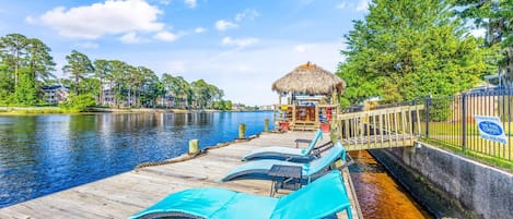 Eine Holzsteg mit Liegestühlen, einem Gazebo mit Strohdach und einem Fluss.