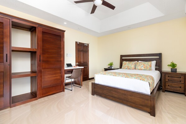 Un dormitorio con cama, escritorio, silla, armario y ventilador de techo.