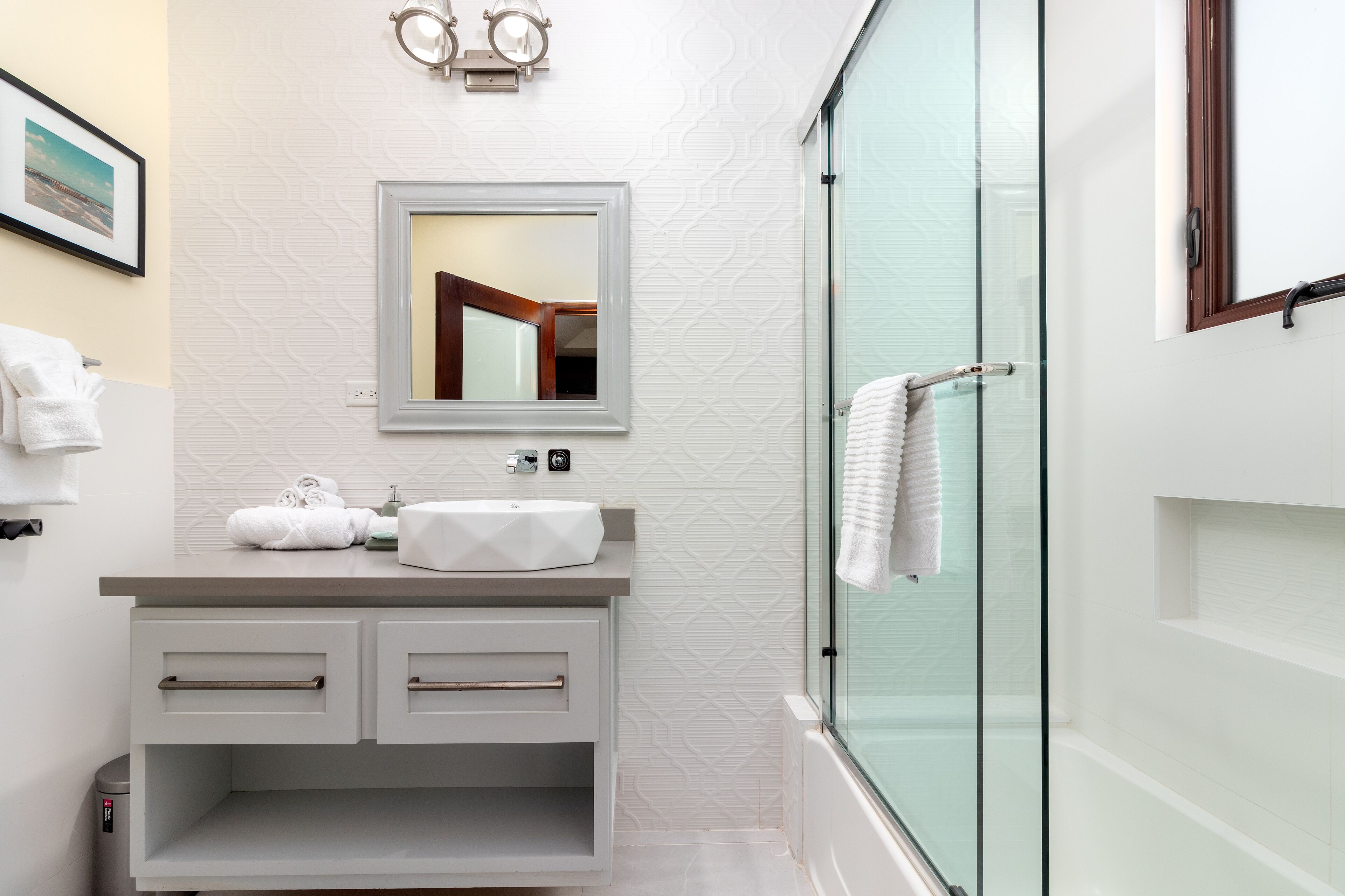 A modern bathroom with a white vanity, a glass shower enclosure, and a framed mirror above the sink.