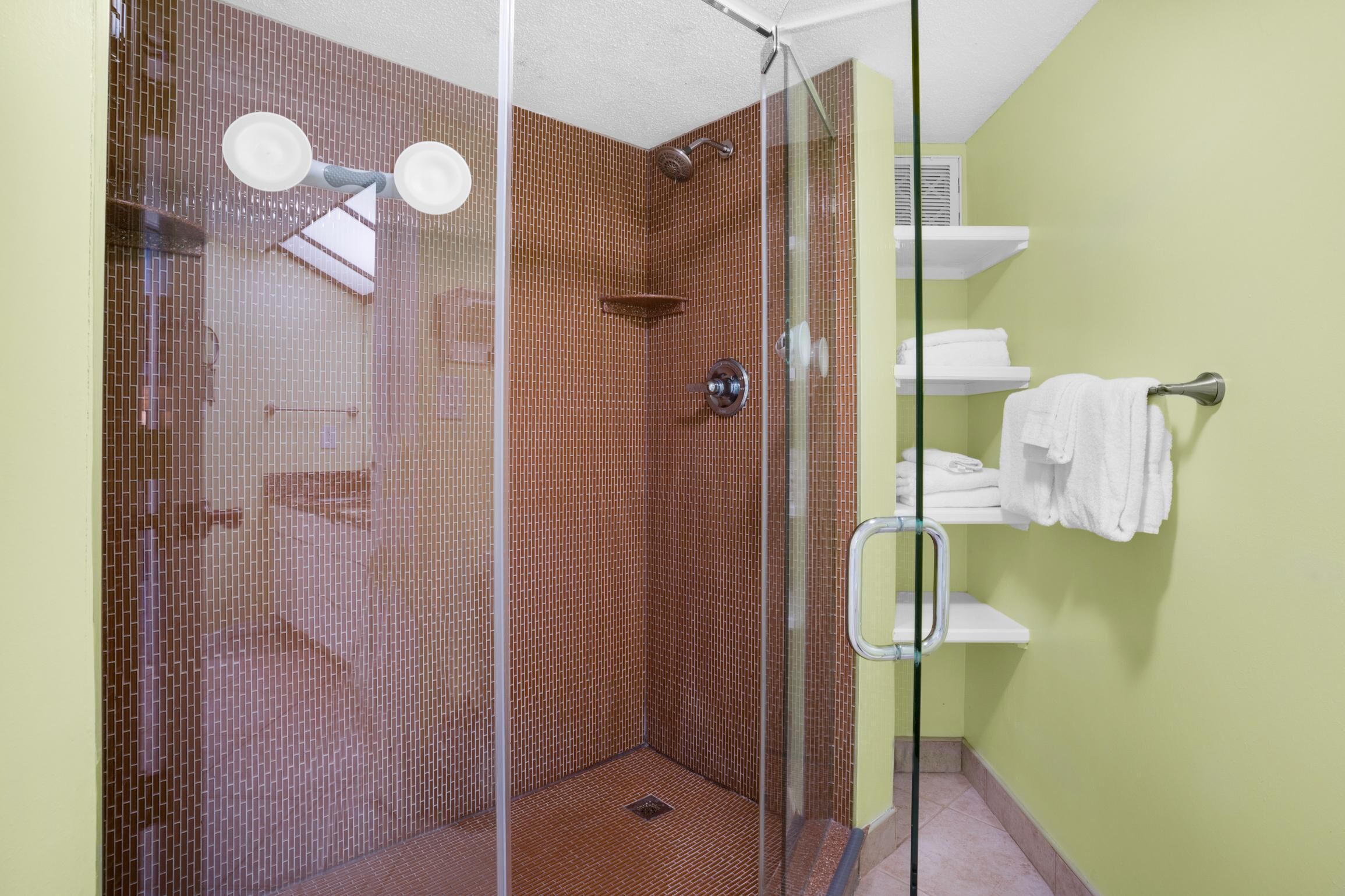 A glass-enclosed shower with a tiled wall, a white towel rack, and a small shelf.