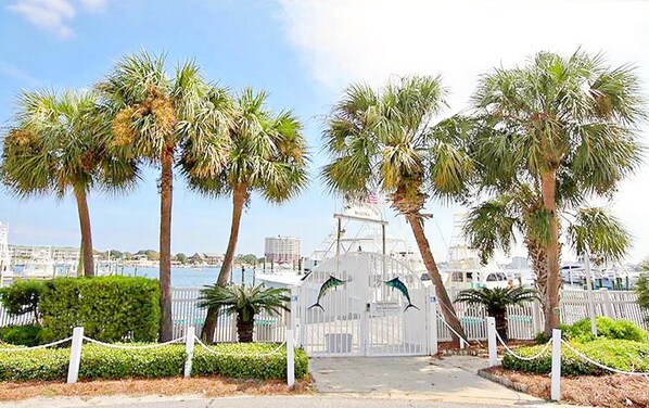 A gated entrance with palm trees and a marina in the background. - East Pass 208 (Destin)