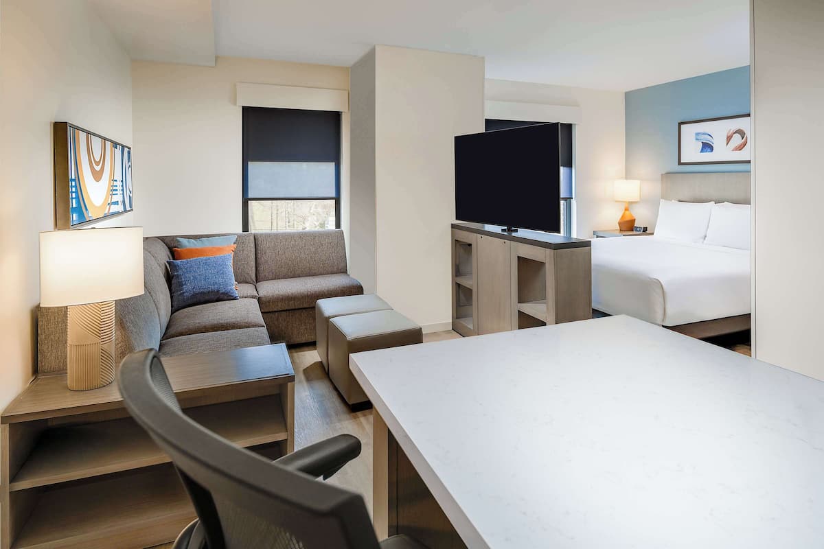 Een moderne hotelkamer met een bank, een televisie, een bed en een eettafel.