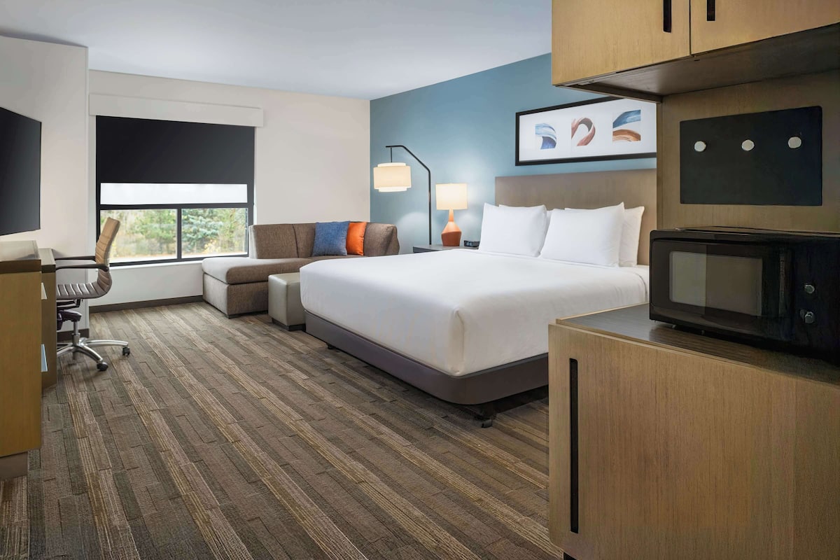 Een hotelkamer met een groot bed, een bureau, een stoel, een televisie en een raam met zonwering.