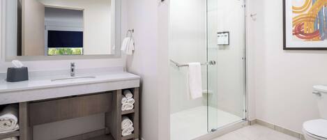 Un baño moderno con ducha de vidrio, un espejo grande y un lavamanos con toallero.
