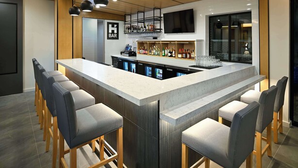 A modern bar area with a marble countertop, bar stools, and a variety of liquor bottles. - Hyatt House Auburn Hills / Detroit (Lake Orion)