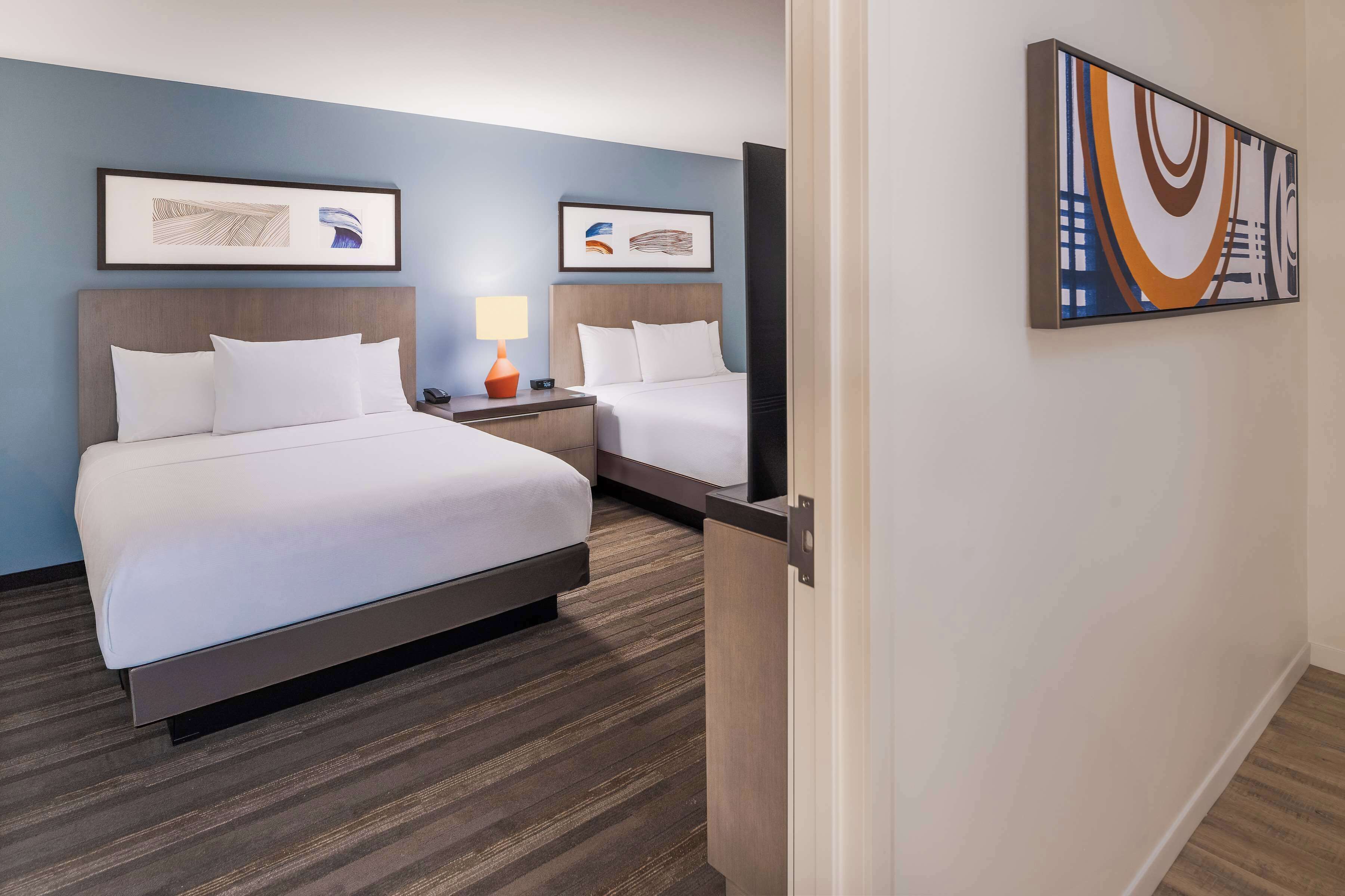 A hotel room with two beds, a nightstand with a lamp, and artwork on the walls.