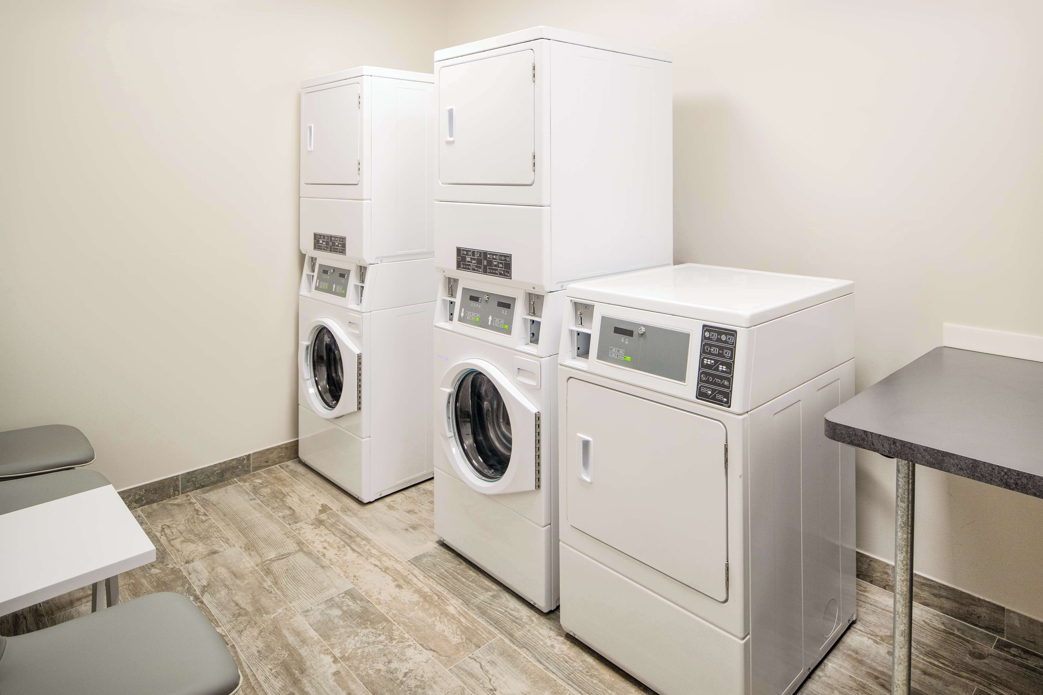 A laundry room with three stacked washers and dryers, a small table, and a bench.