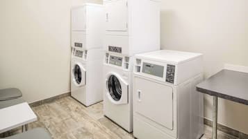A laundry room with three stacked washers and dryers, a small table, and a bench.