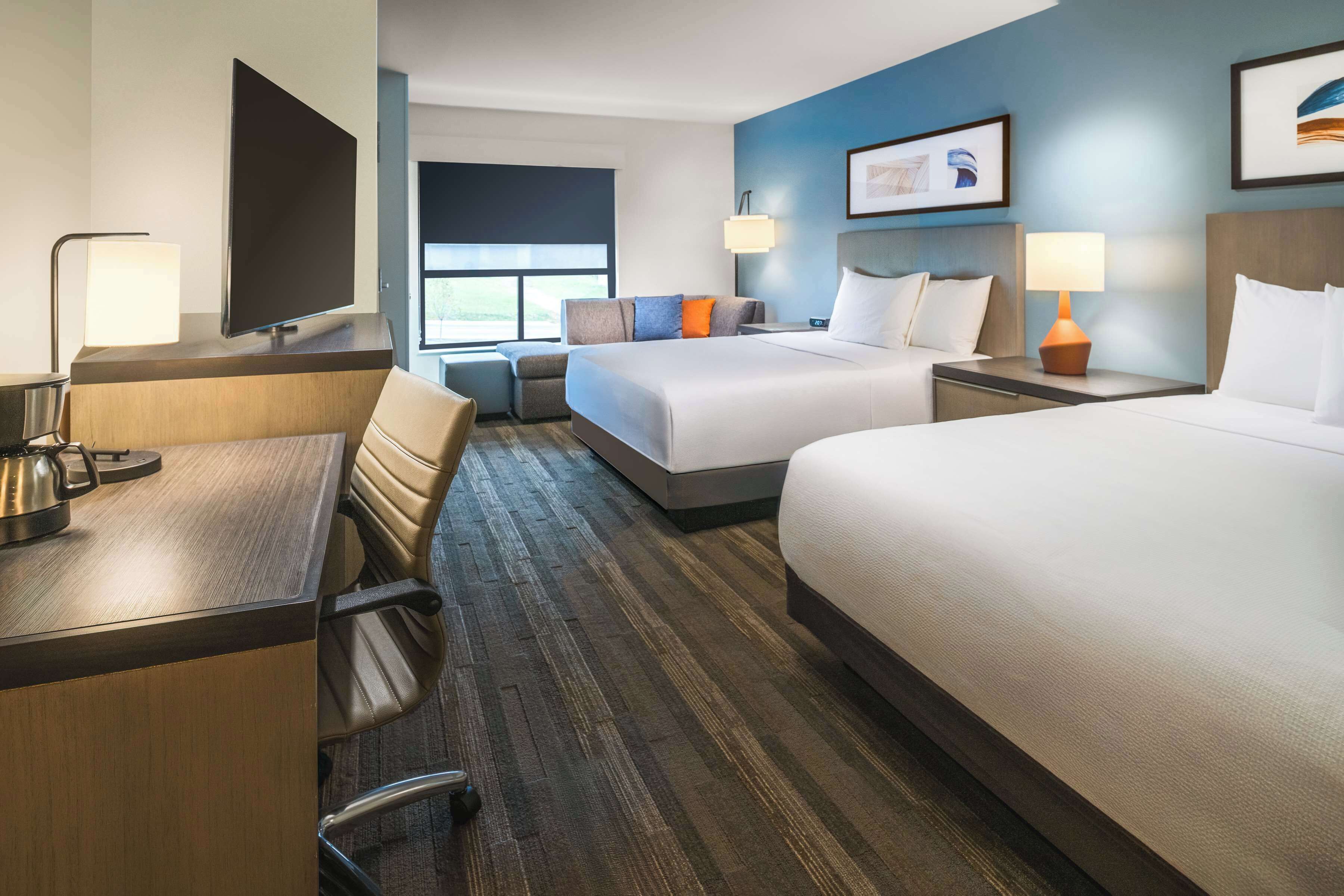 A hotel room with two beds, a desk, a chair, a TV, and a window.