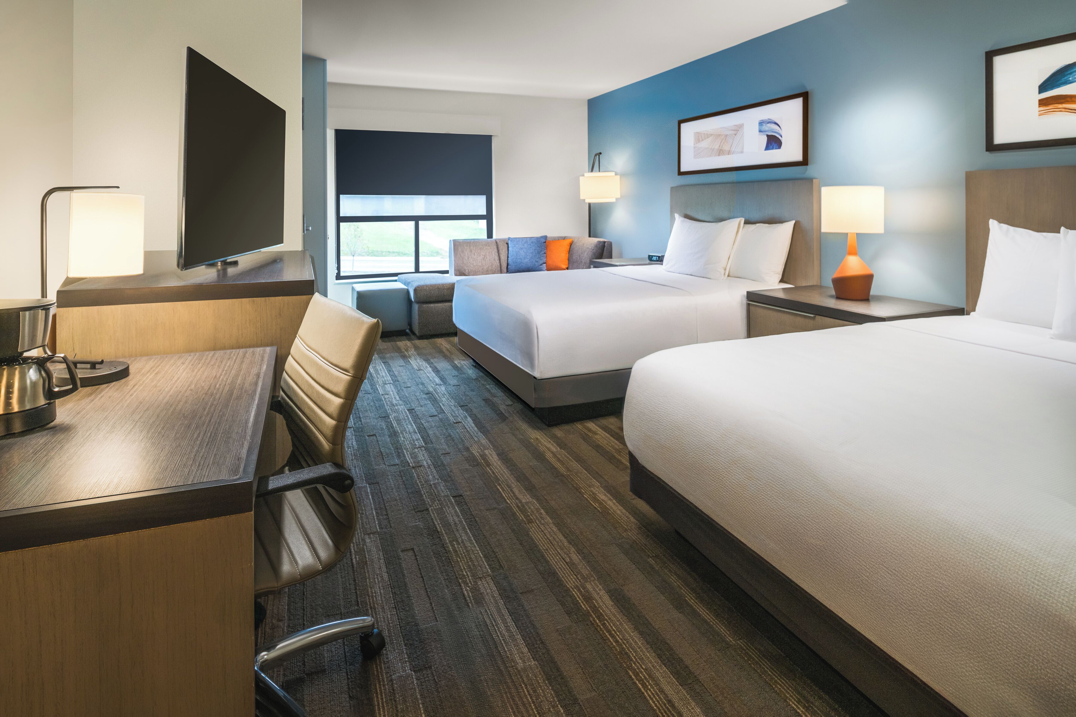 A hotel room with a desk, two beds, a TV, and a window.
