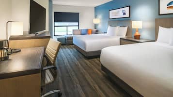 A hotel room with a desk, two beds, a TV, and a window.
