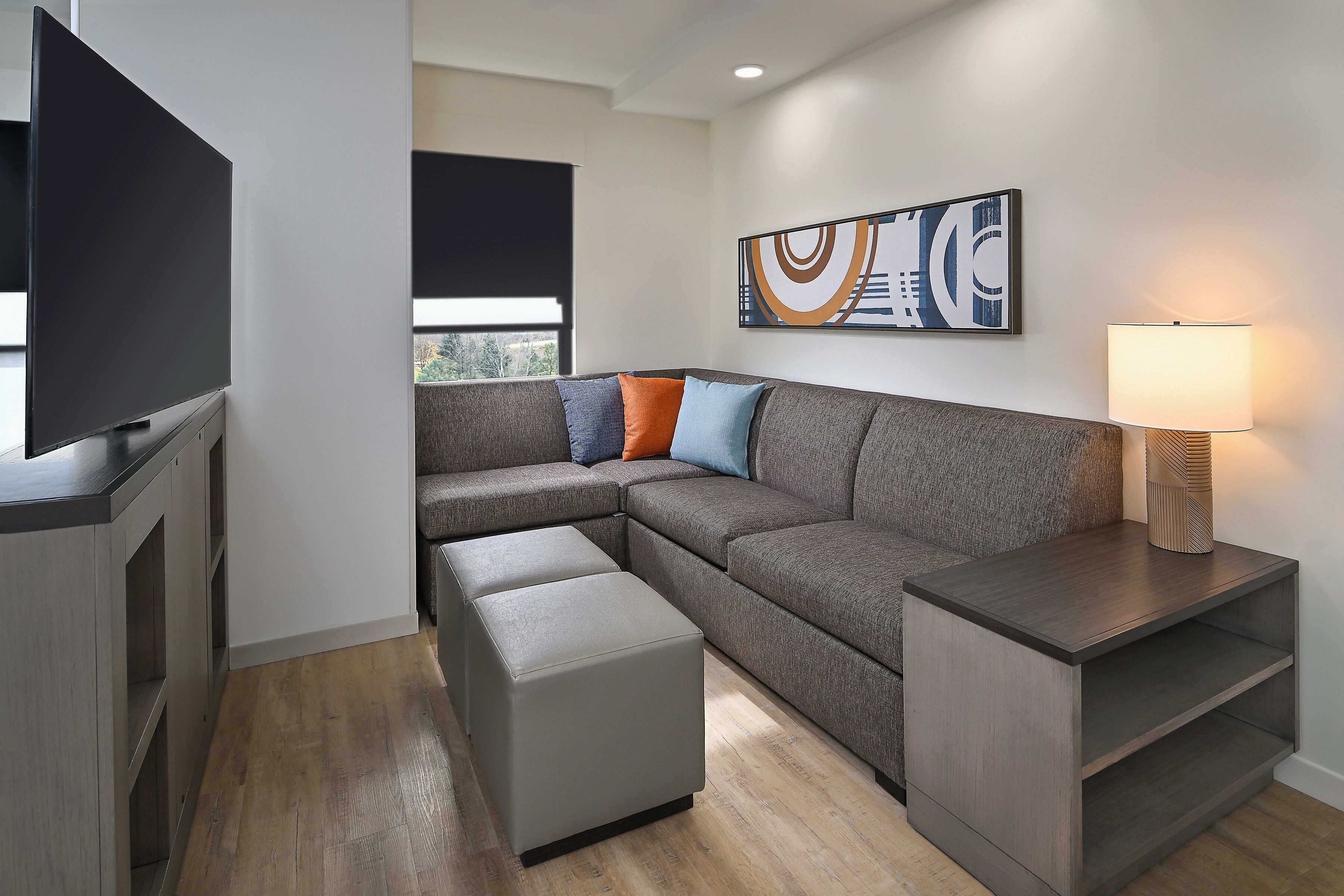 A modern living room with a sectional sofa, ottoman, TV, and a wall-mounted lamp.