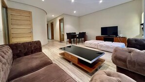 A modern living room with a sofa, a glass-top coffee table, a TV, and a dining area. - Charming two bedroom apartment in the city center

 (Casablanca)