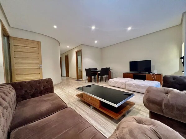 Un salon moderne comprenant un canapé, une table basse avec un plateau en verre, un téléviseur et un coin repas.