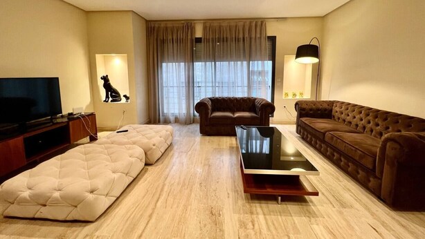 A living room with a flat-screen TV, two sofas, a coffee table, and a large window with curtains. - Charming two bedroom apartment in the city center

 (Casablanca)