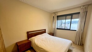 A bedroom with a wooden bed, a nightstand, a window with curtains, and a view of the outside. - Charming two bedroom apartment in the city center

 (Casablanca)