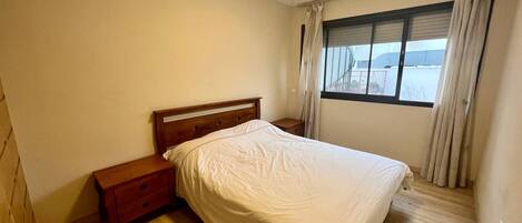 Un dormitorio con una cama de madera, una mesita de noche, una ventana con cortinas y vistas al exterior.