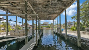 A covered dock area with a boat, wooden pillars, and a view of residential buildings in the background. - Destin-a-tion on the Water (Destin)