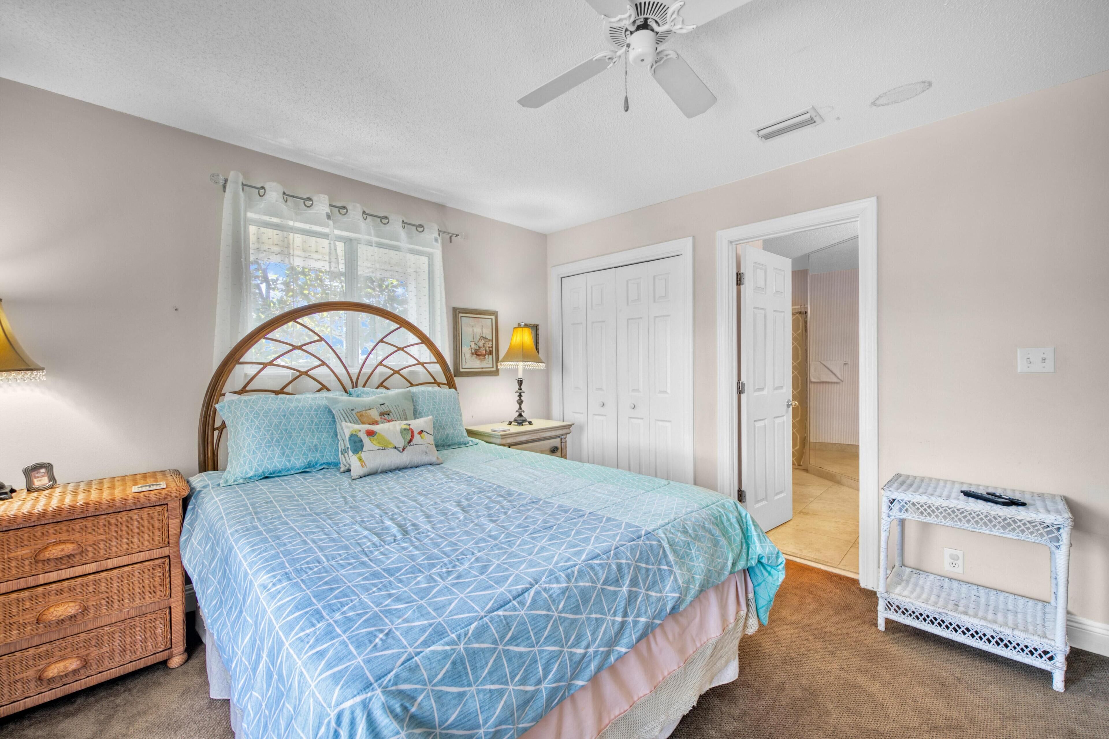 A bedroom with a bed, a nightstand, a wicker dresser, a white side table, and a ceiling fan.