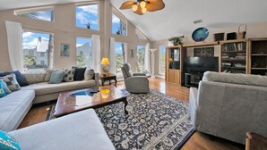 A spacious living room with a large sofa, a coffee table, a patterned rug, and a ceiling fan. - Destin-a-tion on the Water (Destin)