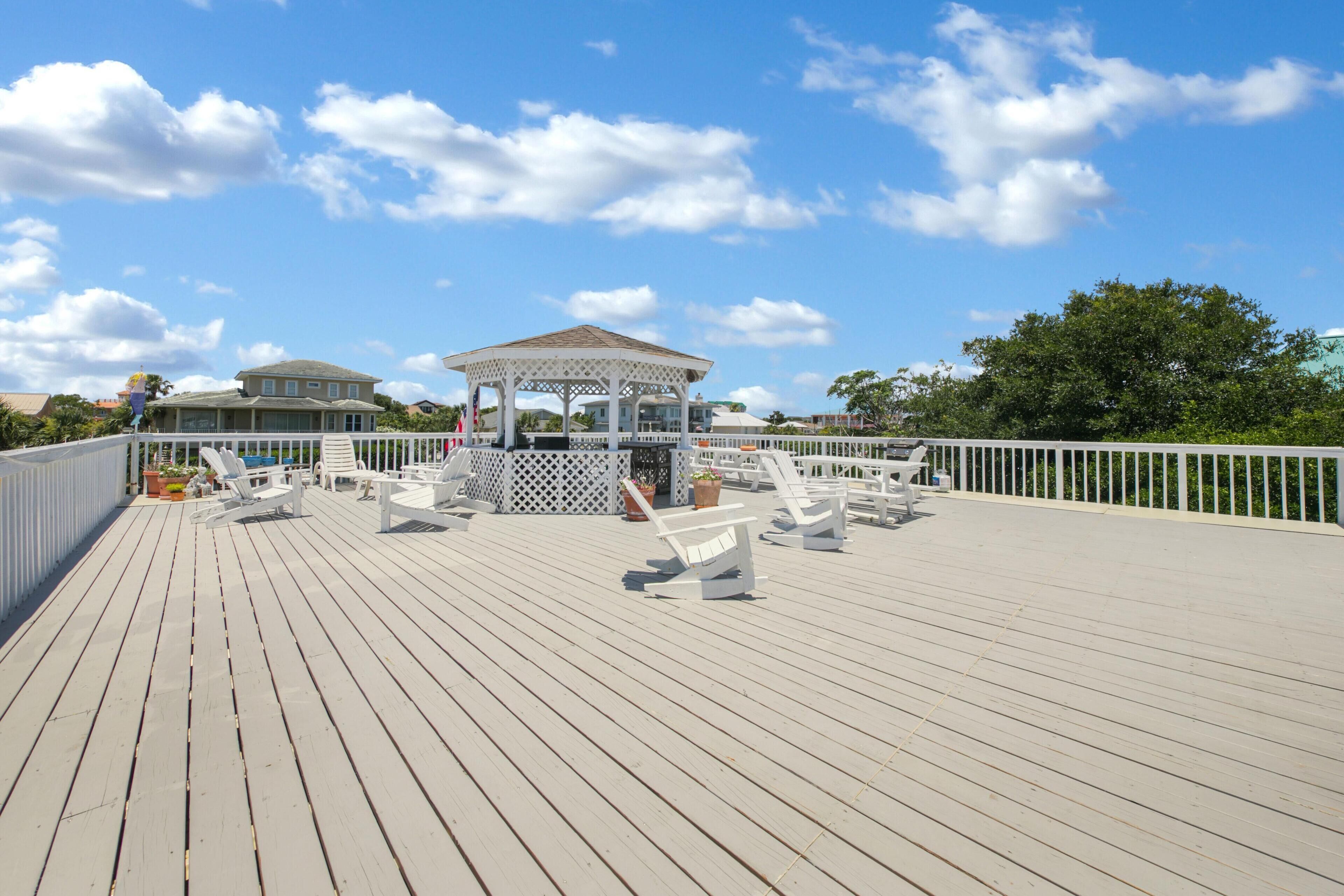 A wooden deck with white lounge chairs and a gazebo.