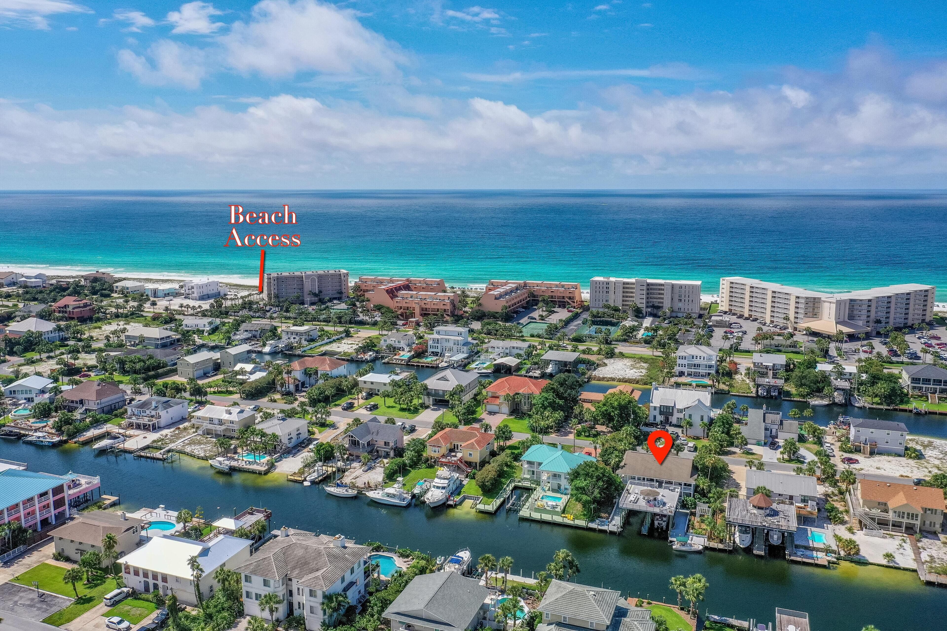 An aerial view of a coastal residential area with a marina, beachfront properties, and a clear view of the ocean.