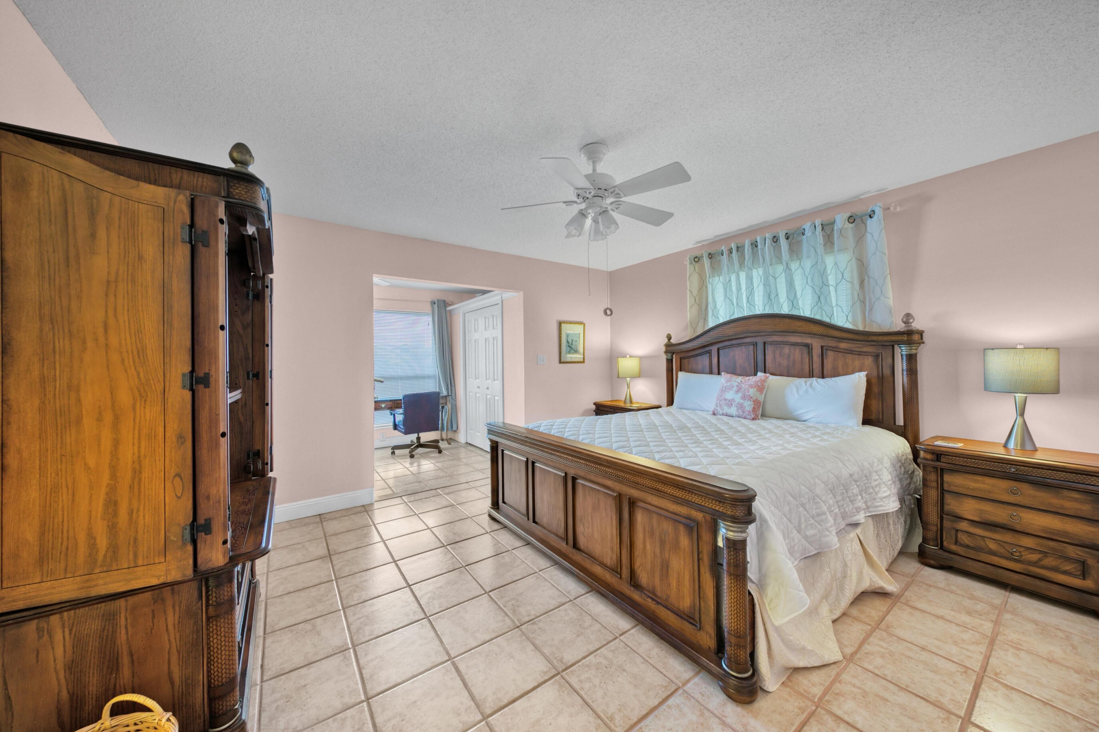 A bedroom with a wooden bed, a nightstand, a lamp, a ceiling fan, and a view of the outside.