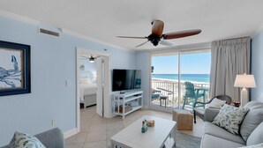 A living room with a TV, a ceiling fan, a sofa, a coffee table, and a balcony with a view of the ocean. - Destin on the Gulf 401 (Destin)