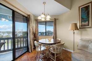 A dining area with a round table and chairs, a chandelier, a view through a glass door, a sofa, and a framed picture on the wall.