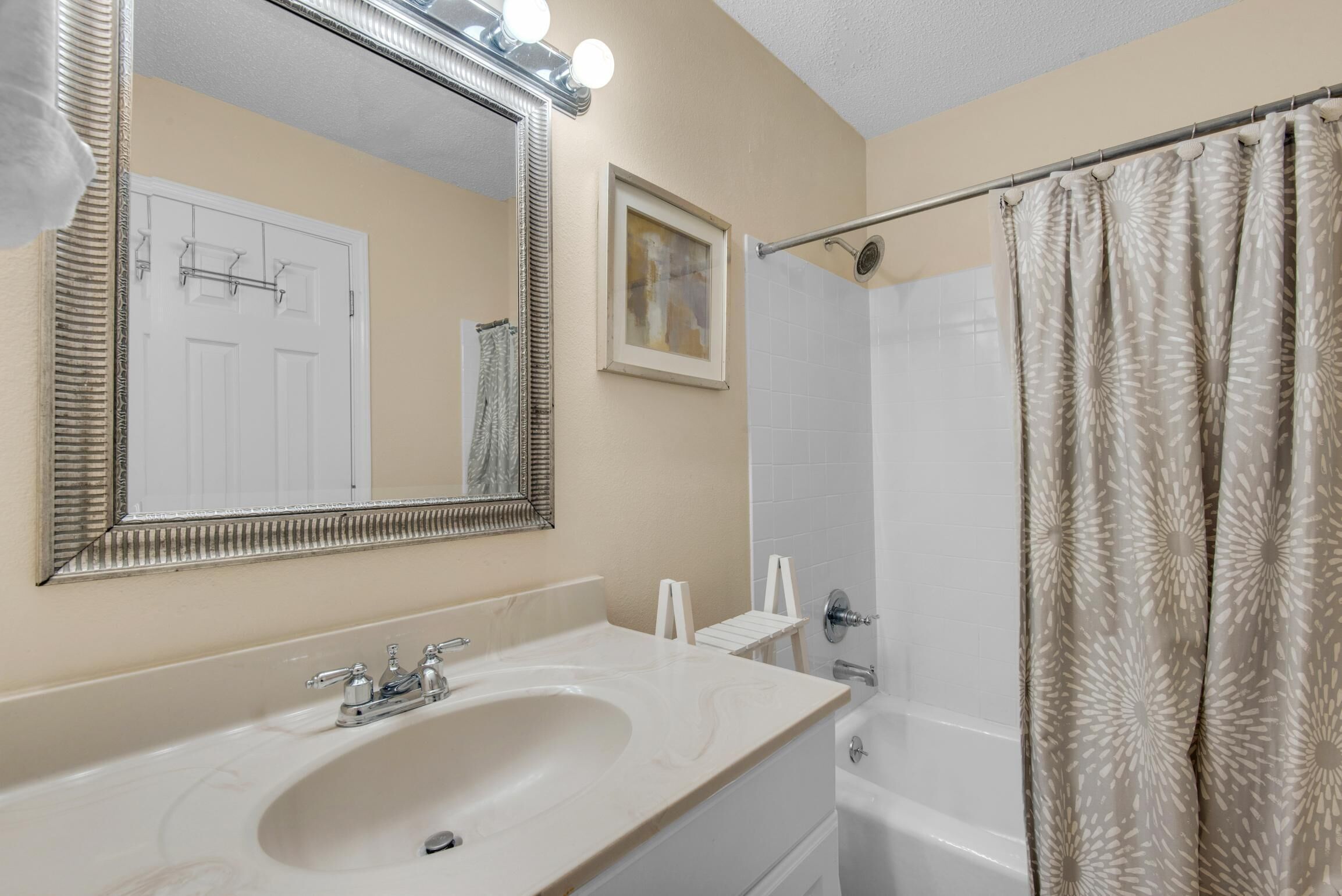 A bathroom with a sink, mirror, shower, and a door.