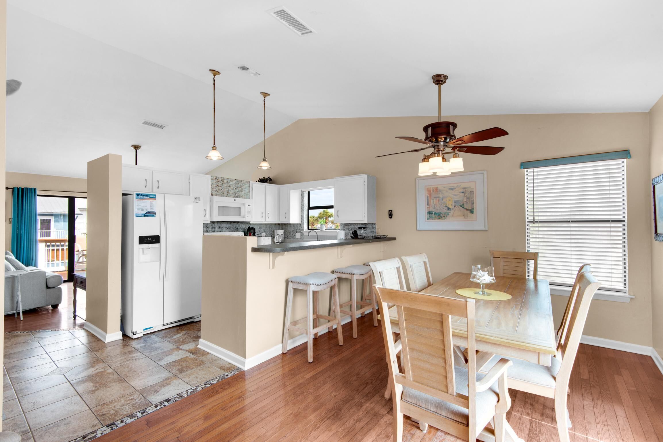 A modern kitchen with white cabinets, a central island with stools, and a dining area with a wooden table and chairs.