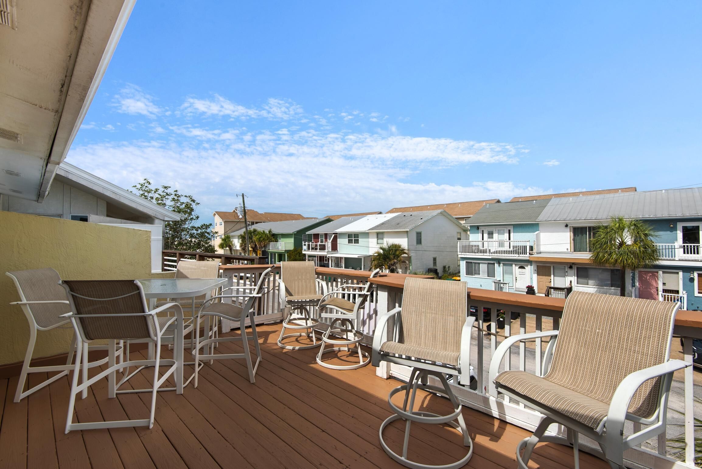 A wooden deck with white wicker chairs and a table, overlooking a row of colorful buildings.