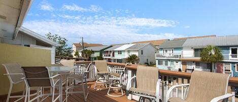 A wooden deck with white wicker chairs and a table, overlooking a row of colorful buildings.