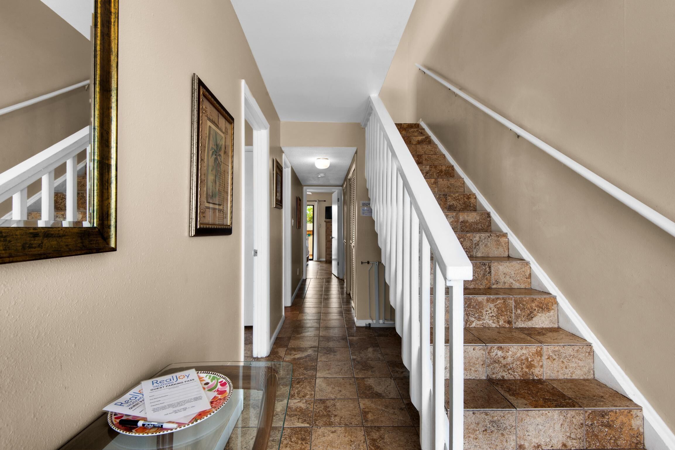 A hallway with a staircase, a glass table with a plate and papers, and framed pictures on the walls.