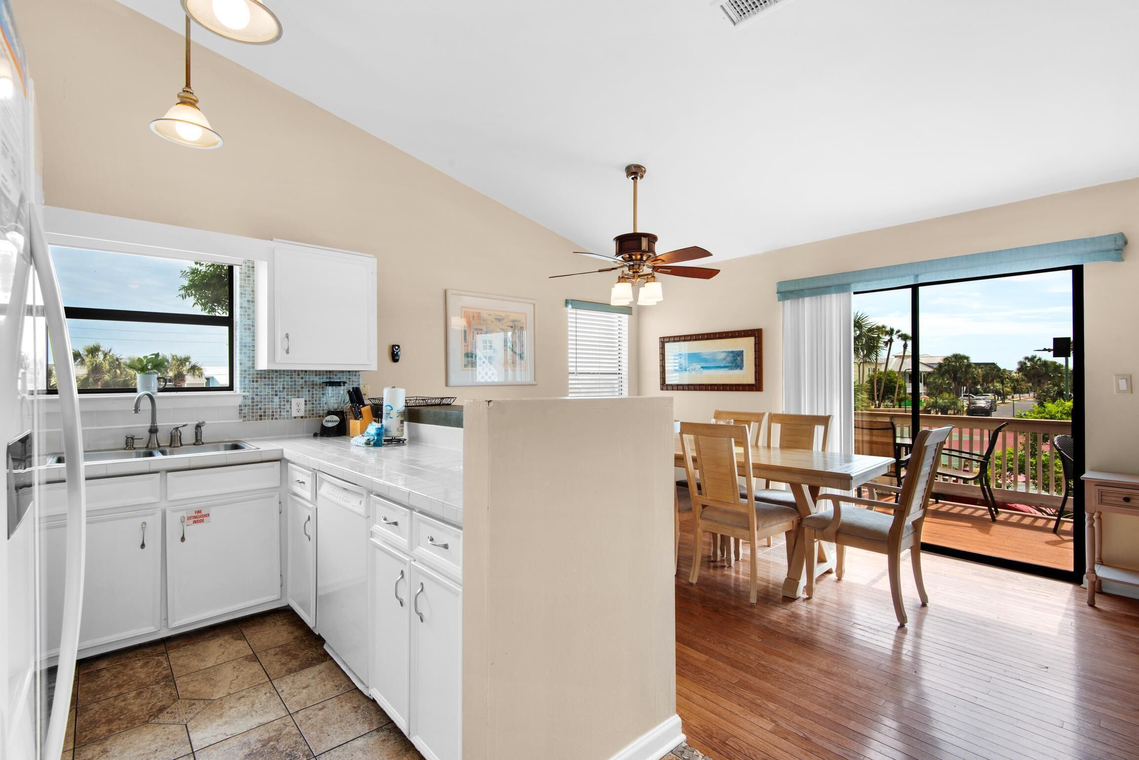 A modern kitchen with white cabinets, a dining area with wooden furniture, and a balcony with a view.