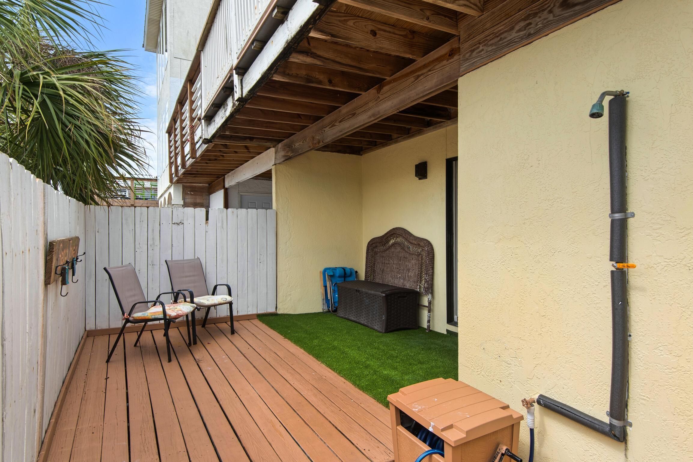 A wooden deck with two chairs and a small table, a covered seating area, and a hose connected to a wall.