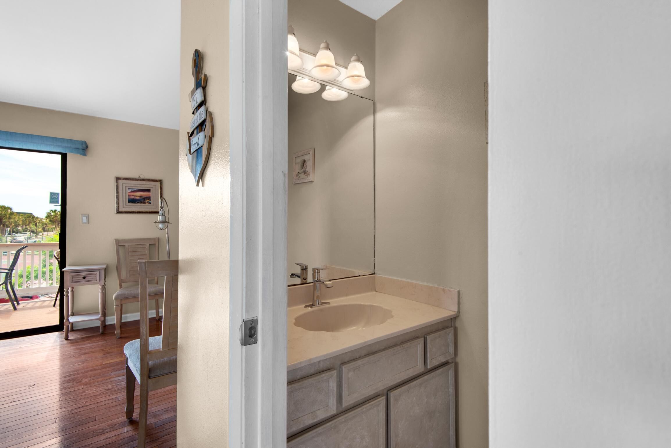A bathroom with a large mirror, a sink, and a vanity. There is a chair and a small table with a lamp.