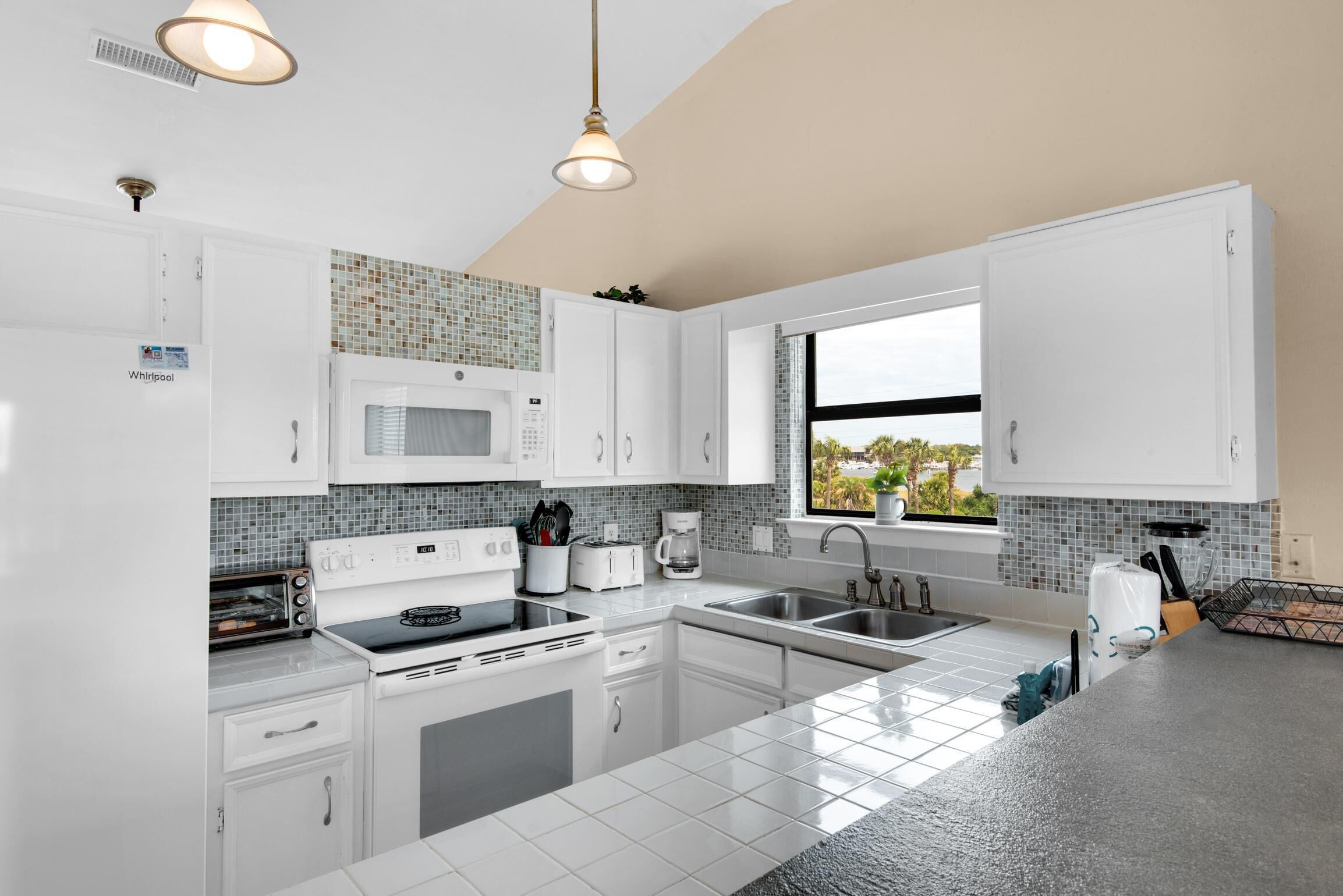 A modern kitchen with white cabinets, a microwave, a stove, and a sink.