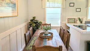 A dining area with a wooden table, chairs, a ceiling fan, and a window with blinds.
