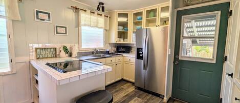 Una cocina compacta con armarios blancos, un microondas integrado y un refrigerador de acero inoxidable.