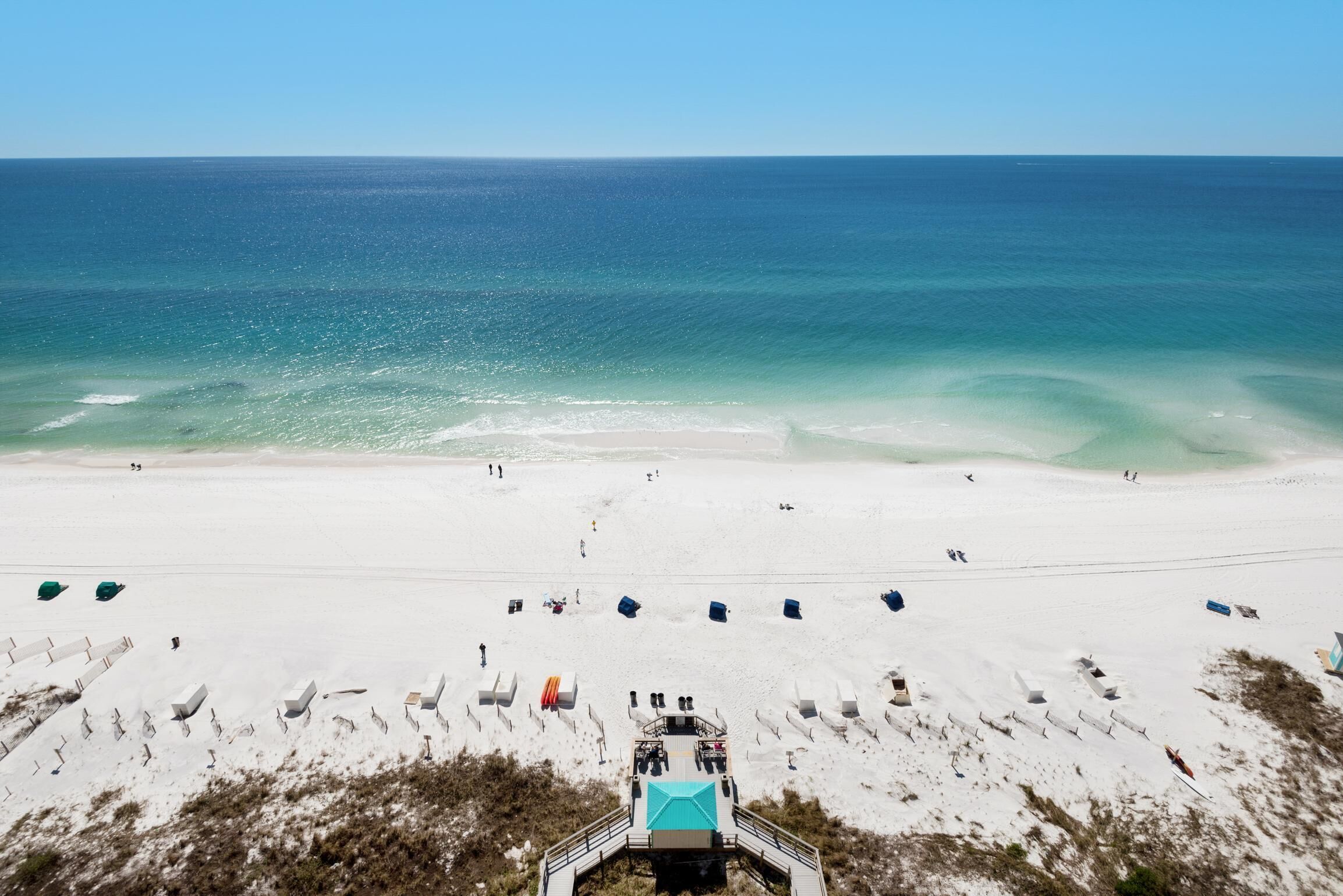 A beach with a clear view of the ocean, a sandy beach, and a structure with a turquoise roof.