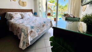 A bedroom with a large bed, a glass table, and a view of a pool and greenery outside.