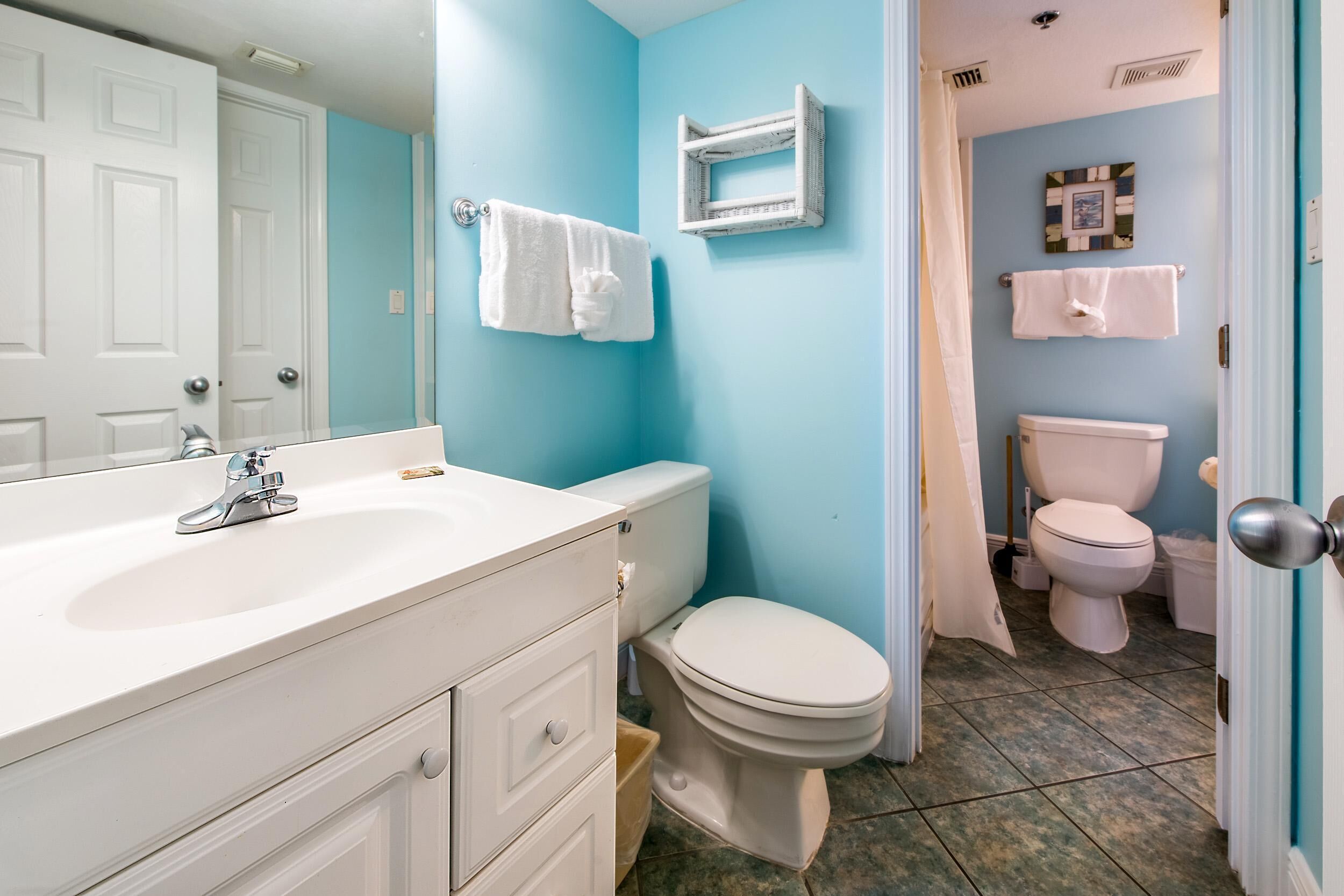 A bathroom with a white sink, two toilets, and a blue wall.