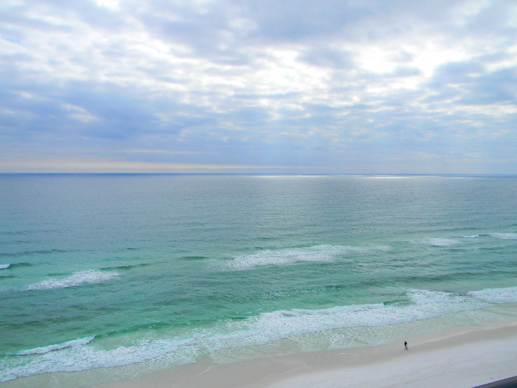 A beach with clear turquoise water and a person walking along the shore.
