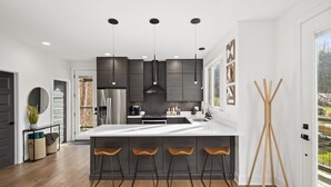 Uma cozinha moderna com armários escuros, uma ilha grande com banquetas, iluminação pendente e vista para o exterior.