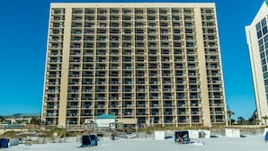 Een hoog hotel met meerdere balkons, een ligging aan het strand en een helderblauwe lucht.