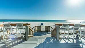 Een houten terras met witte stoelen dat uitkomt op een strand.